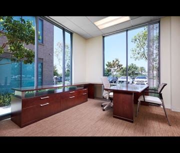 Irvine apartment for rent - A room with a desk and chairs with a view of trees and a building outside the window.