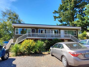 Portland apartment for rent - A silver car is parked in front of a house with a tree in the front yard.