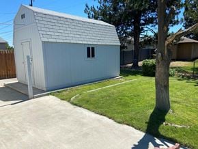 Richland apartment for rent - A small white shed with a grey roof is situated in a grassy area.
