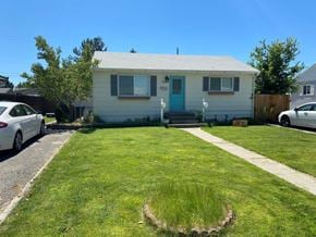 Richland apartment for rent - A small white house with a blue door is surrounded by a green lawn.