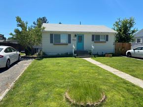 Richland apartment for rent - A small white house with a blue door is surrounded by a grassy lawn and a sidewalk.