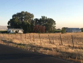 Prosser house for rent - A house is situated in a field with a fence running along the roadside.