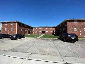 Omaha apartment for rent - A parking lot in front of a brick building with two cars parked.