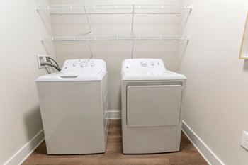 A washer and dryer in a room with a white wall and a shelf