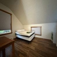 Sitka house for rent - A bed with a white sheet and a green pillow is in a room with wooden floors.