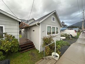 Sitka house for rent - A house with a grey siding and a white door is surrounded by a green lawn and a wooden deck.