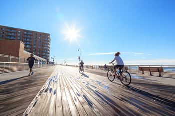 A sunny day at the beach with people jogging and biking on the boardwalk.