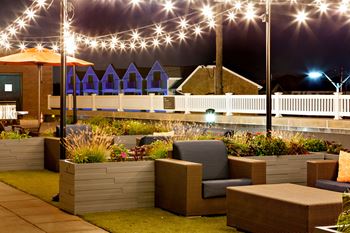 A patio area with a white picket fence and a building in the background.