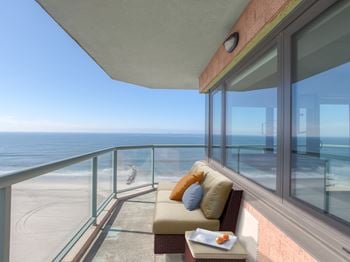 A balcony with a couch and a tray of food overlooking the beach.