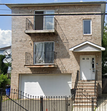 Newark apartment for rent - A two-story brick house with a white garage door and a black metal fence.