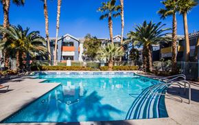 Las Vegas apartment for rent - A swimming pool surrounded by palm trees and a building in the background.