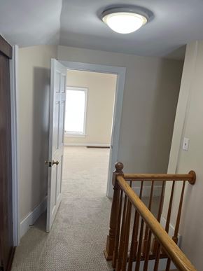 Grayslake apartment for rent - A hallway with a light on the ceiling and a wooden railing on the right.