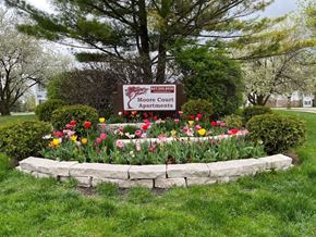 Grayslake apartment for rent - A sign for Moore Court Apartments is surrounded by flowers and greenery.