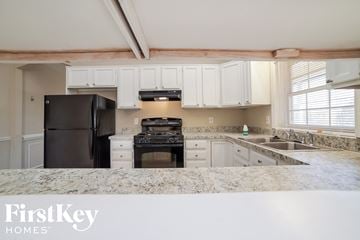 Dallas house for rent - a kitchen with white cabinets and black appliances and granite counter tops