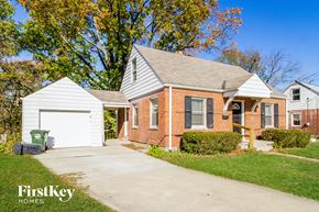 Cincinnati house for rent - A brick house with a white garage door and a green trash can in front of it.