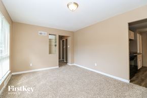 Florissant house for rent - A spacious room with a carpeted floor and a kitchen area visible in the background.