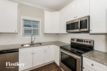 Newnan house for rent - a kitchen with white cabinets and black appliances and granite counter tops