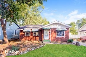 Indianapolis house for rent - A house with a red brick exterior and a white door is surrounded by a well-kept lawn and trees.