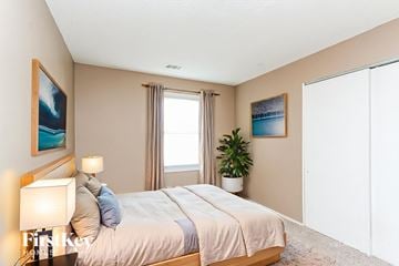Indianapolis house for rent - A bedroom with a large bed, a nightstand with a lamp, and a plant on the windowsill.
