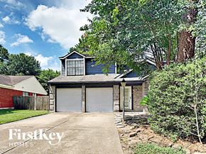 Spring house for rent - A house with a garage is surrounded by trees and bushes.
