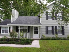 North Charleston house for rent - A house with a grey siding and a white door is surrounded by greenery.