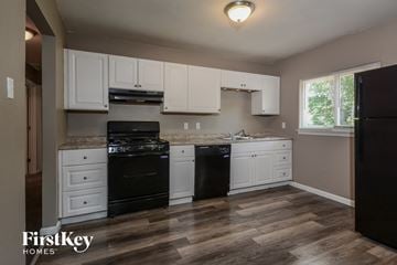 Florissant house for rent - A kitchen with a black fridge, white cabinets and a wooden floor.