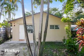 Hallandale Beach house for rent - A small house with a white door and windows is surrounded by trees and plants.