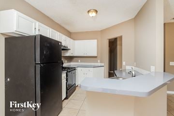 Sebastian house for rent - a kitchen with white cabinets and a black refrigerator