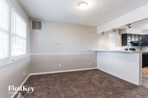 Monrovia house for rent - A room with a carpeted floor and a kitchen area in the background.