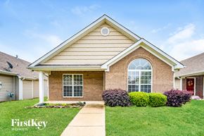 Calera house for rent - A house with a red door and a brick facade is surrounded by green bushes.