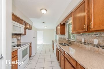 Sanford house for rent - a kitchen with wooden cabinets and white tile floors and a sink