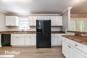 Summerville house for rent - a kitchen with white cabinets and granite counter tops and a black refrigerator