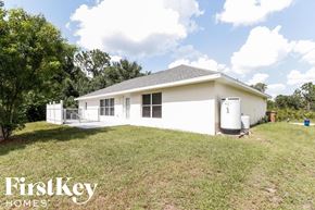 Lehigh Acres house for rent - A white house with a grey roof is surrounded by green grass and trees.