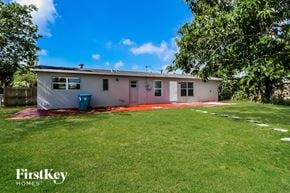 Boynton Beach house for rent - A house with a white and pink exterior is surrounded by a green lawn.