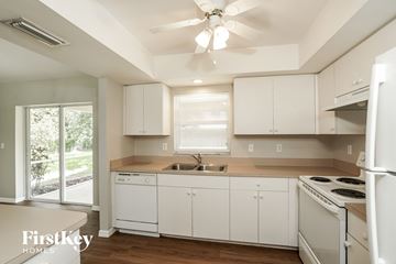 Cape Coral house for rent - a kitchen with white cabinets and white appliances and a ceiling fan