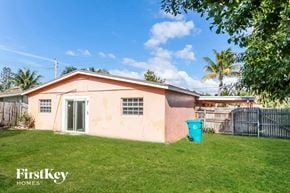Boynton Beach house for rent - A small house with a pinkish exterior is shown with a green trash can in front of it.