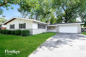 Florissant house for rent - A white house with a garage is surrounded by greenery.