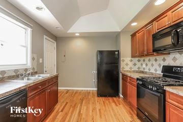 Bensenville house for rent - a kitchen with wooden cabinets and black appliances and a wood floor
