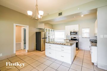 Hollywood house for rent - A kitchen with white cabinets and appliances, a black refrigerator, and a chandelier hanging from the ceiling.