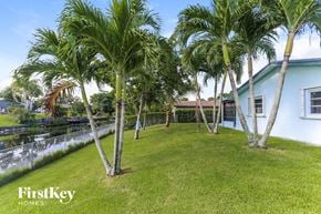 Coconut Creek house for rent - A white house with a blue roof is surrounded by palm trees.