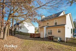 Wake Forest house for rent - A house with a white and beige exterior is surrounded by trees and has a brown bench in front of it.