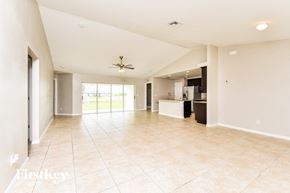 Cape Coral house for rent - an empty living room with a kitchen and a ceiling fan