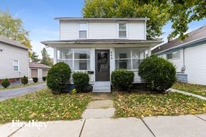 Aurora house for rent - A white house with a black front door and two bushes on either side.