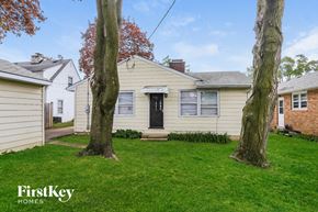 Waukegan house for rent - A house with a black door is surrounded by trees and grass.