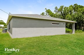 Port St. Lucie house for rent - the backyard of a white brick house with grass and trees