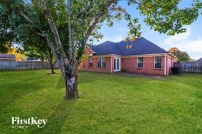 Cordova house for rent - A tree stands in a grassy yard in front of a brick house with a blue roof.