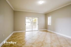 Homestead house for rent - A spacious room with beige tiled flooring and a sliding glass door leading to a backyard.