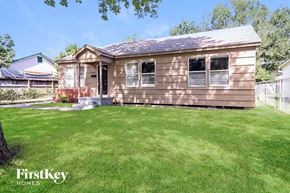 Baytown house for rent - A small house with a brown siding and a white door is surrounded by a green lawn.