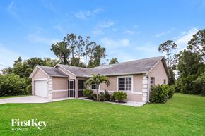Lehigh Acres house for rent - a small pink house with a green lawn and trees
