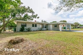 Cocoa house for rent - A white house with a red roof is surrounded by trees and grass.